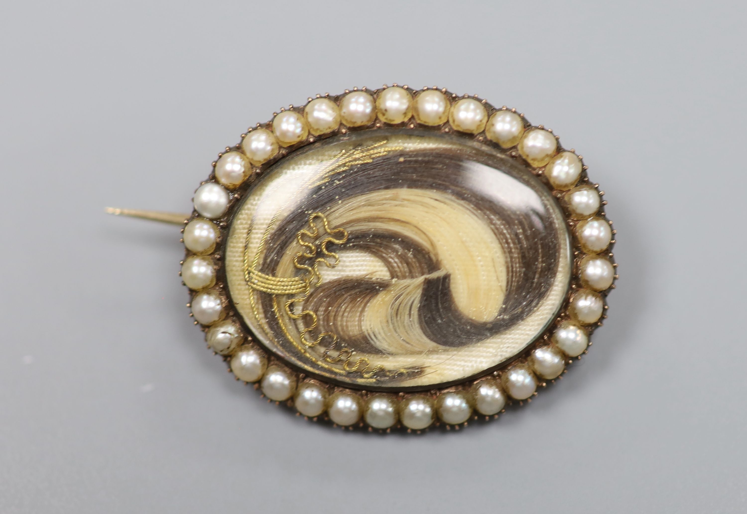 A Victorian yellow metal and split pearl set oval locket, with lock of plaited hair below a glazed panel, 27mm, gross 6.6 grams.